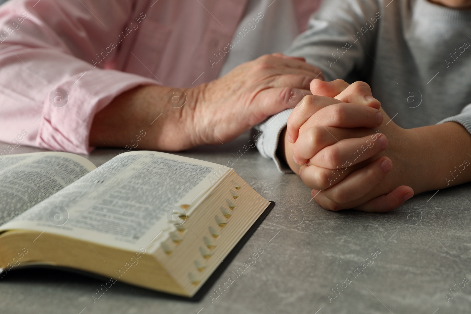 Photo of Boy and his godparent praying together at grey table, closeup