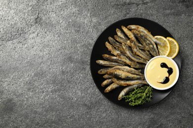 Photo of Plate with delicious fried anchovies, lemon, microgreens and sauce on grey table, top view. Space for text