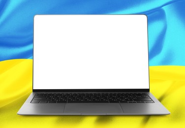 Laptop with blank screen and Ukrainian national flag on background