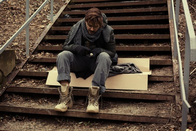 Poor young man sitting on stairs outdoors