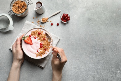 Woman eating tasty yogurt with berries and granola at table, top view