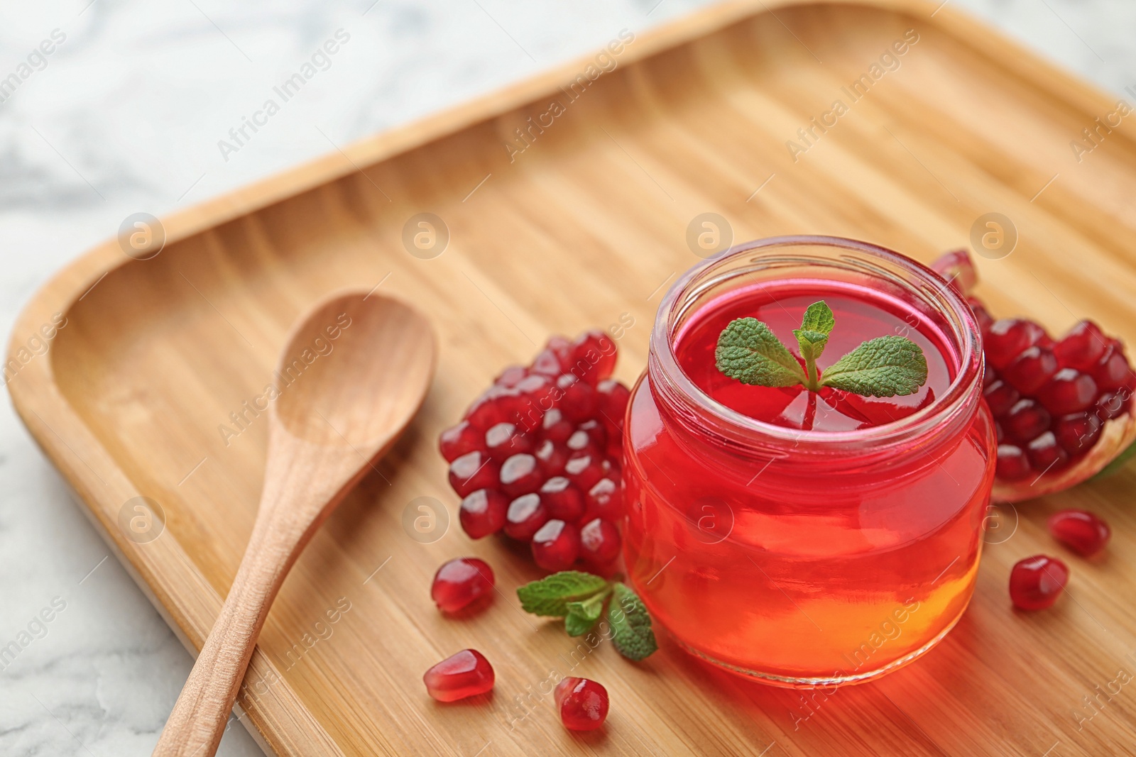 Photo of Tray with jar of fruit jelly, pomegranate seeds and spoon on table, space for text