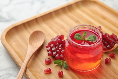 Photo of Tray with jar of fruit jelly, pomegranate seeds and spoon on table, space for text