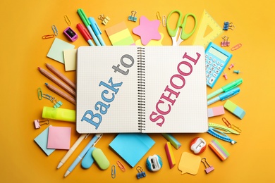 Image of Notebook with text Back To School surrounded by different stationery on yellow, flat lay