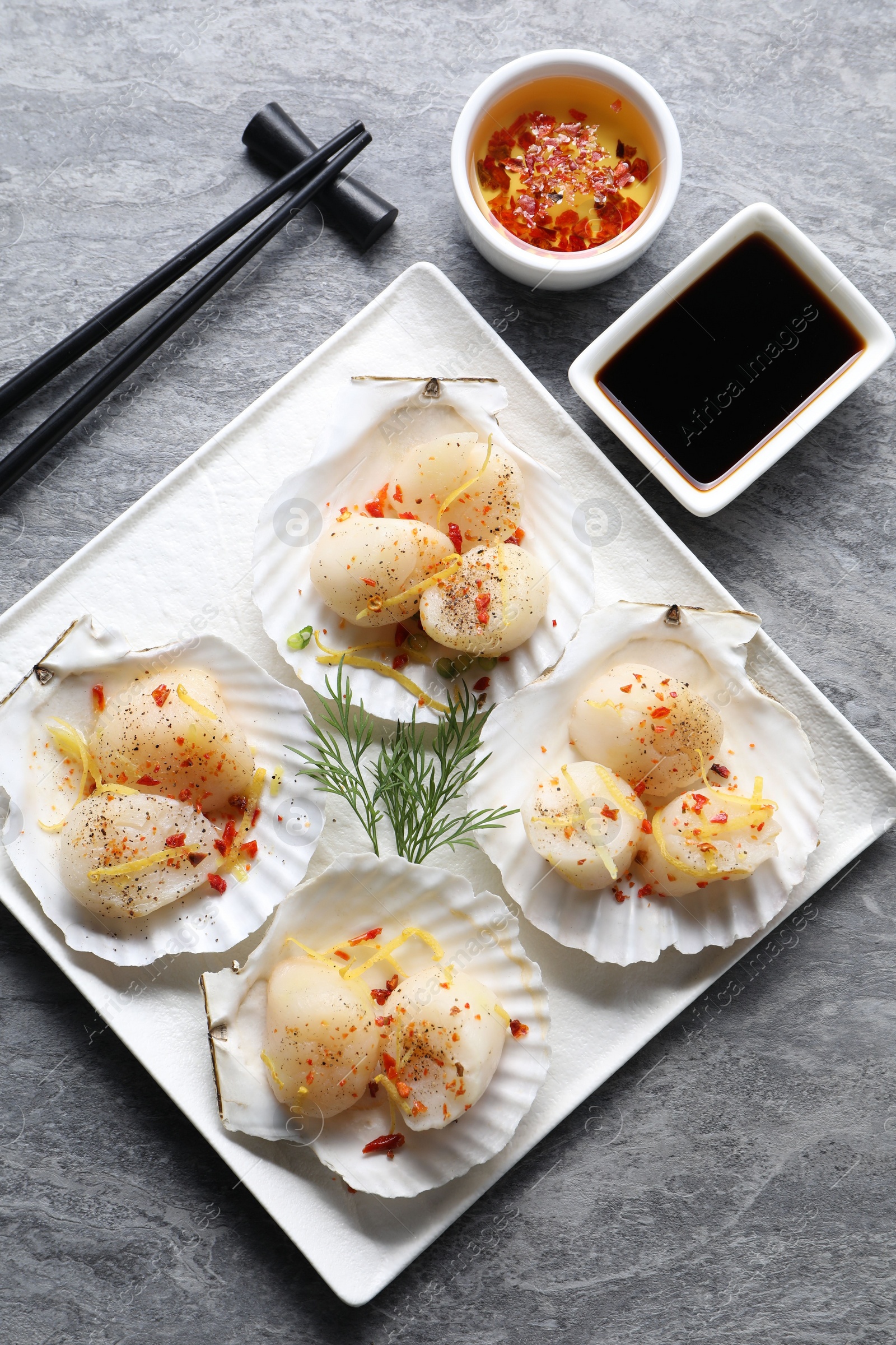 Photo of Raw scallops with spices, dill, lemon zest, shells and soy sauce on grey marble table, flat lay