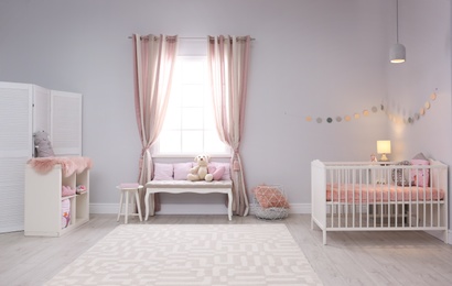 Photo of Baby room interior with comfortable crib and indoor bench