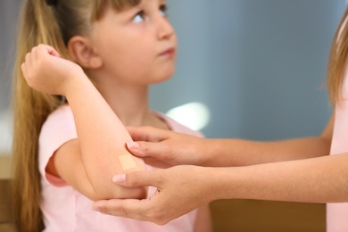 Woman applying plaster on girl's elbow indoors, closeup view