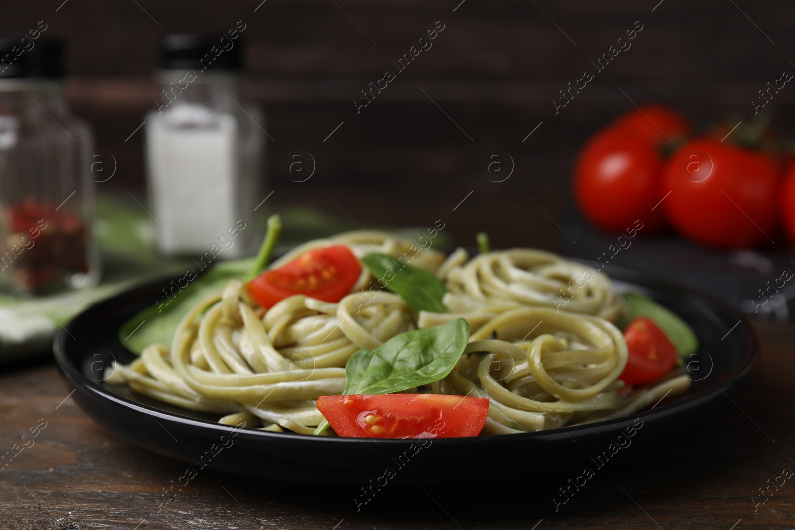 Photo of Tasty pasta with spinach and tomatoes on wooden table, closeup