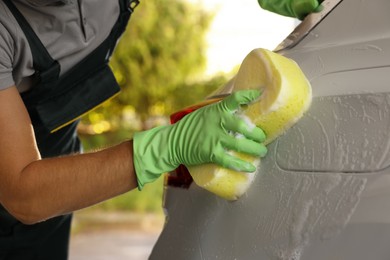 Worker washing auto with sponge at outdoor car wash, closeup