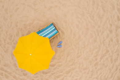 Yellow beach umbrella, sunbed and flip flops on sandy coast, aerial view. Space for text