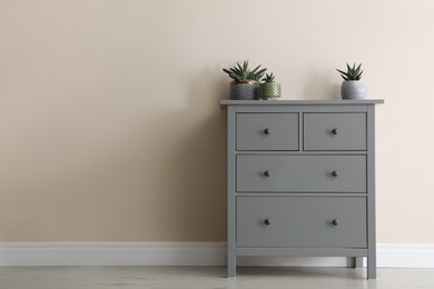 Photo of Grey chest of drawers with houseplants near beige wall. Space for text