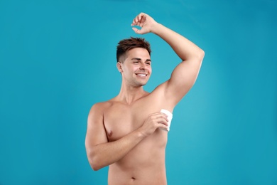 Photo of Young man applying deodorant to armpit on blue background
