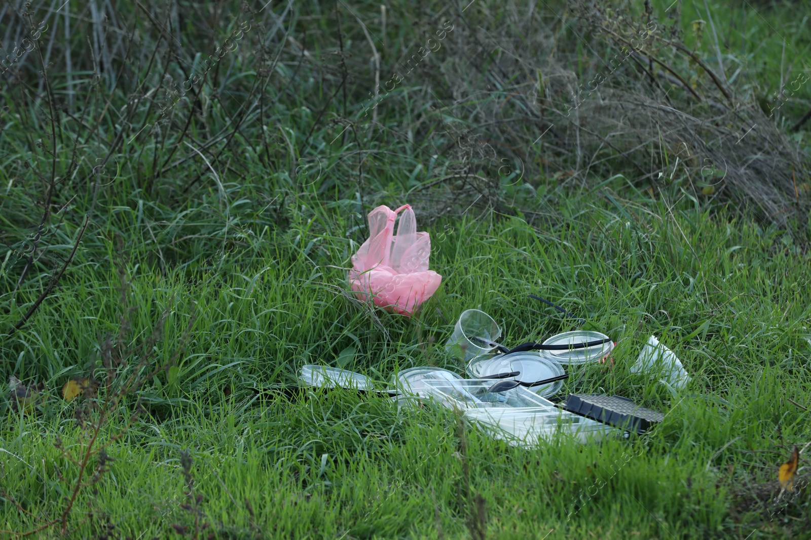 Photo of Used plastic tableware and bag on grass outdoors, space for text. Environmental pollution concept