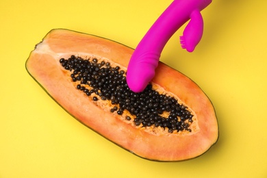 Photo of Half of papaya and purple vibrator on yellow background, top view. Sex concept