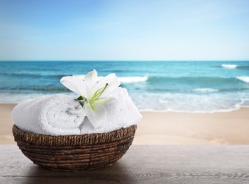 Image of Spa holiday. Fresh towels and lily flower on wooden table against seascape, space for text