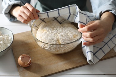 Woman covering dough with napkin at white wooden table, closeup