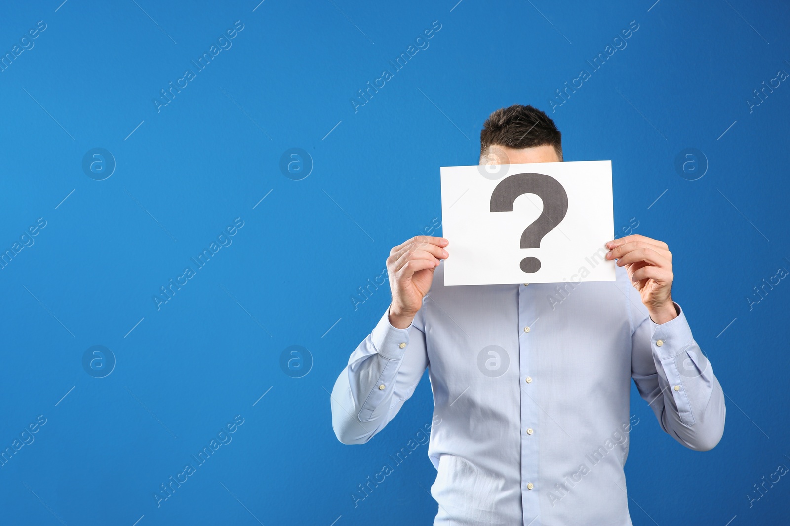 Photo of Man holding paper with question mark on blue background, space for text