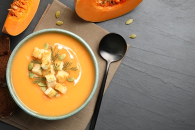 Photo of Delicious pumpkin soup in bowl served on black table, flat lay. Space for text