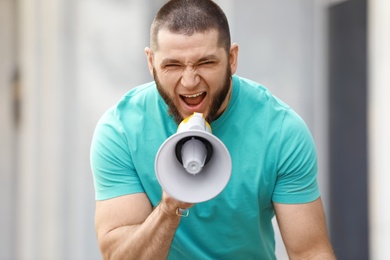 Image of Emotional young man with megaphone outdoors. Protest leader