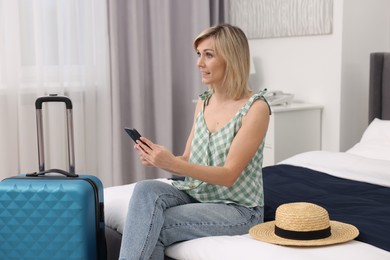 Photo of Smiling guest with smartphone relaxing on bed in stylish hotel room
