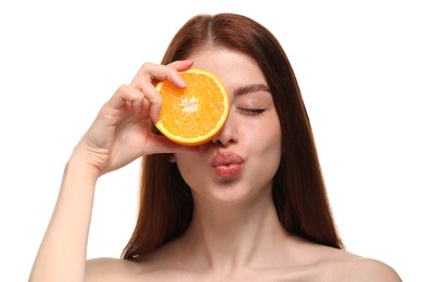 Beautiful woman covering eye with half of orange and sending air kiss on white background