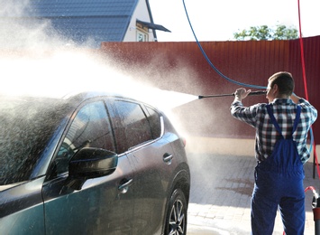 Worker cleaning automobile with high pressure water jet at car wash