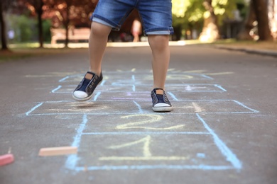 Photo of Little child playing hopscotch drawn with colorful chalk on asphalt