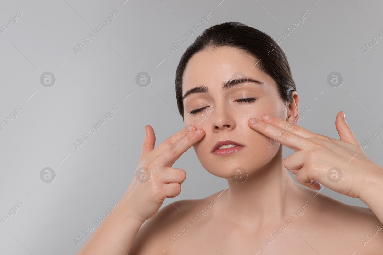 Photo of Young woman massaging her face on grey background. Space for text