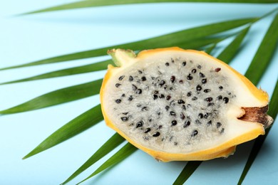 Photo of Delicious cut dragon fruit (pitahaya) and tropical leaf on light blue background, closeup