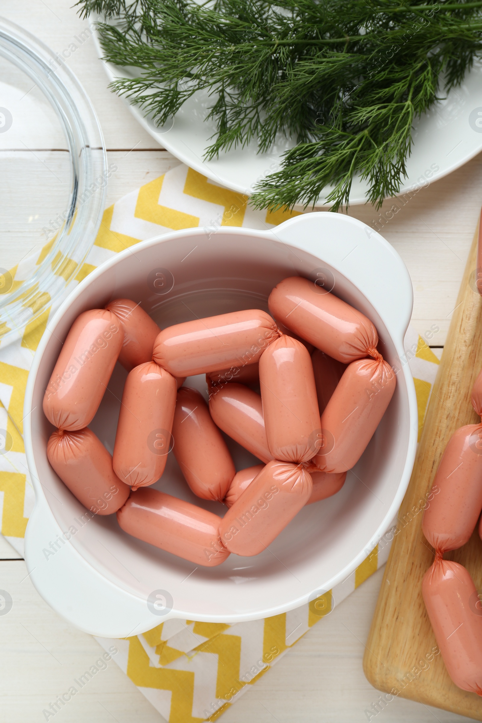 Photo of Bowl of delicious sausages and dill on white wooden table, flat lay