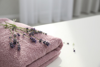 Photo of Folded clean towel and lavender flowers on white table indoors, closeup. Space for text