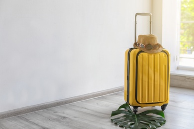Photo of Bright yellow suitcase with hat and sunglasses indoors