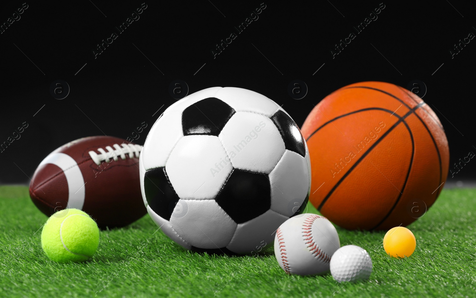 Photo of Many different sports balls on green grass against black background