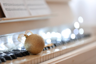Photo of Beautiful golden bauble and fairy lights on piano keys, space for text. Christmas music