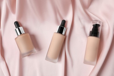 Photo of Bottles of skin foundation on pink cloth, flat lay. Makeup product