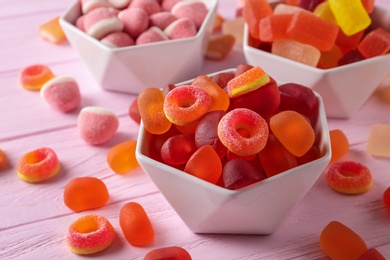 Bowls of tasty jelly candies on pink wooden table, closeup