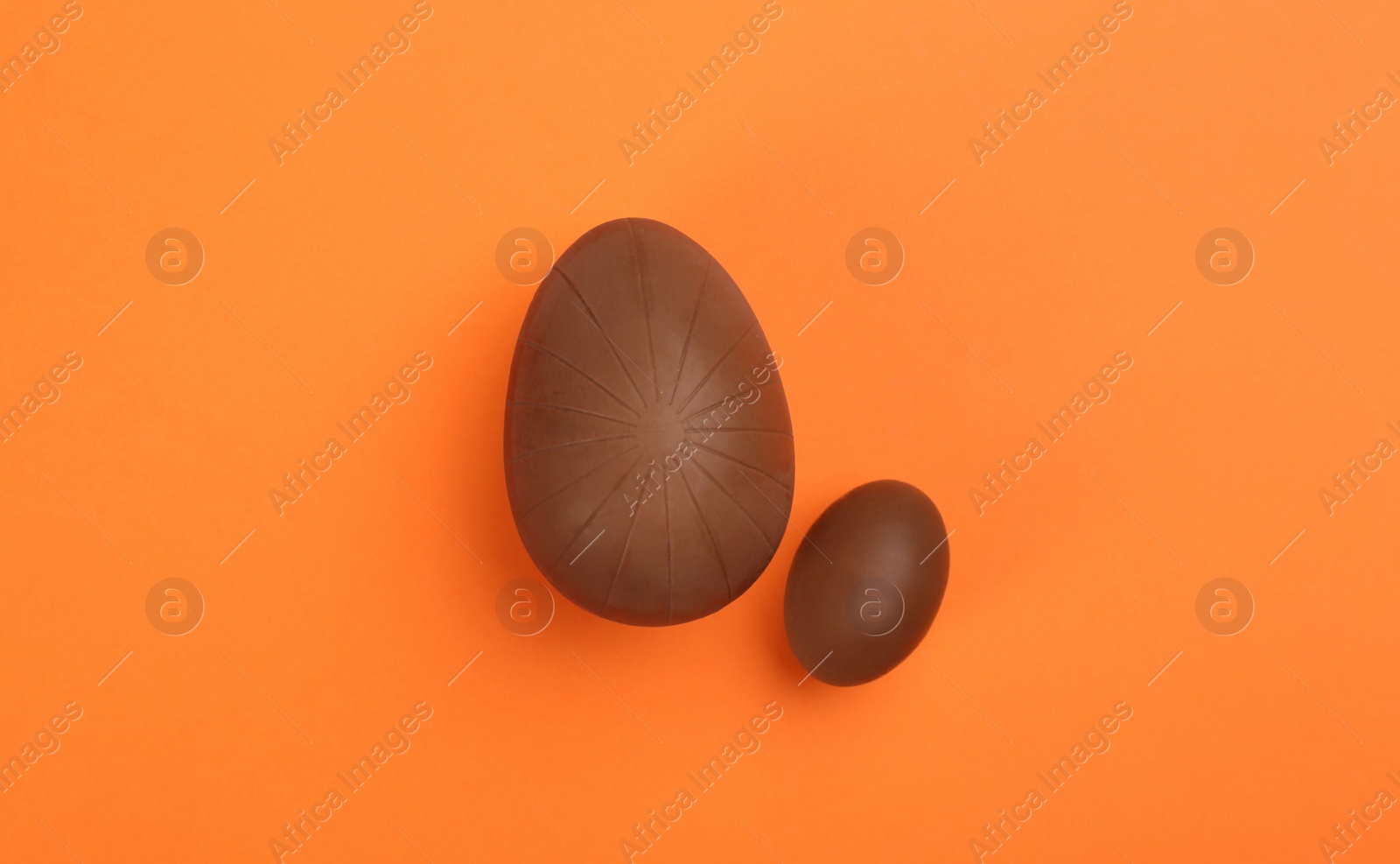 Photo of Sweet chocolate eggs on orange background, flat lay