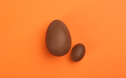 Photo of Sweet chocolate eggs on orange background, flat lay