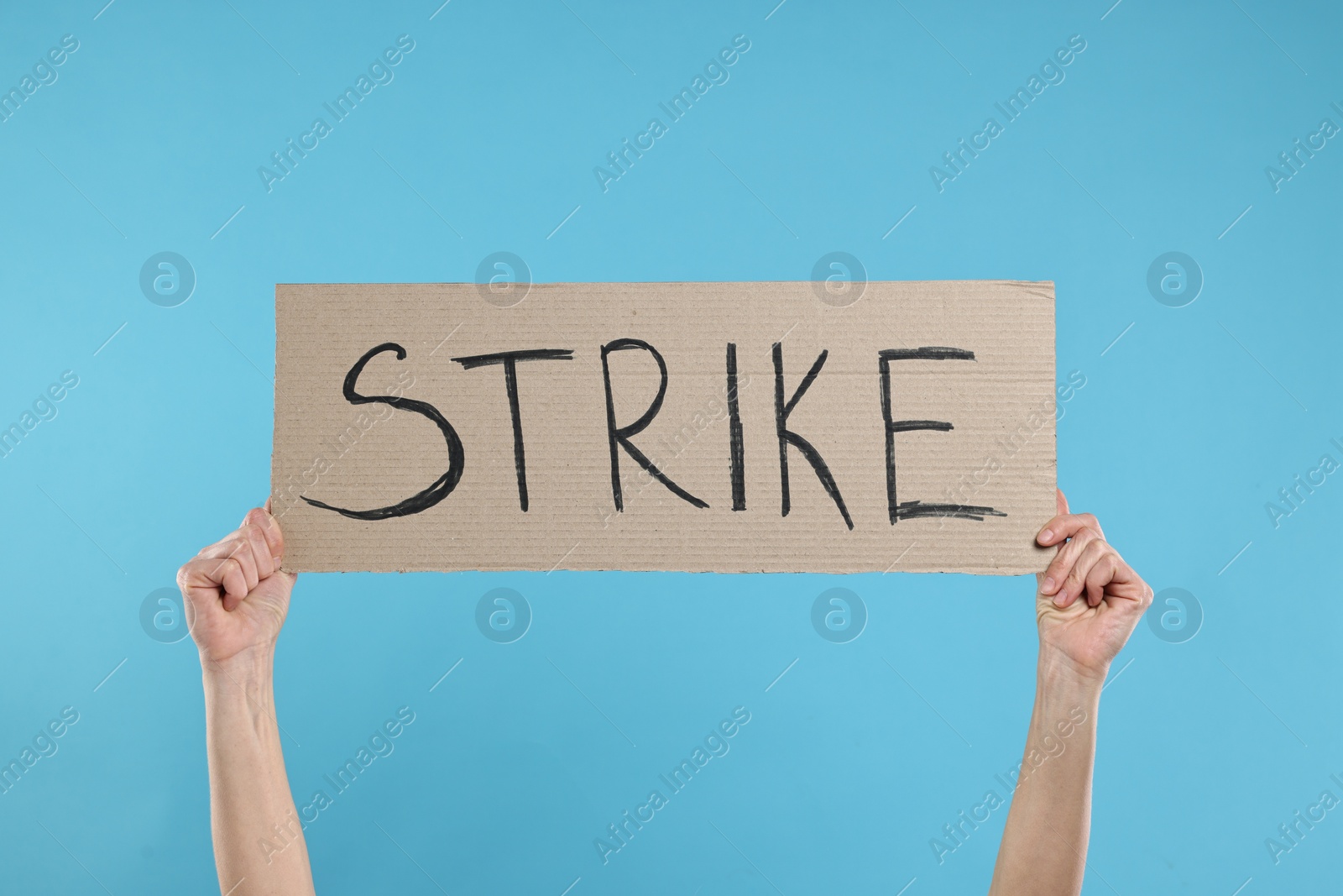 Photo of Woman holding cardboard banner with word Strike on light blue background, closeup