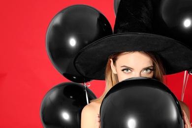 Photo of Beautiful woman wearing witch costume with balloons for Halloween party on red background