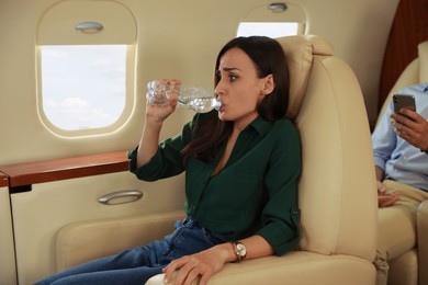Photo of Nervous young woman with aviophobia drinking water in airplane