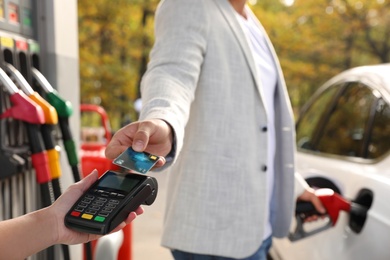 Photo of Man fills the car and paying with credit card at gas station, closeup