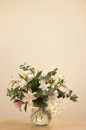 Photo of Bouquet of beautiful lily flowers in vase on wooden table against beige background, space for text