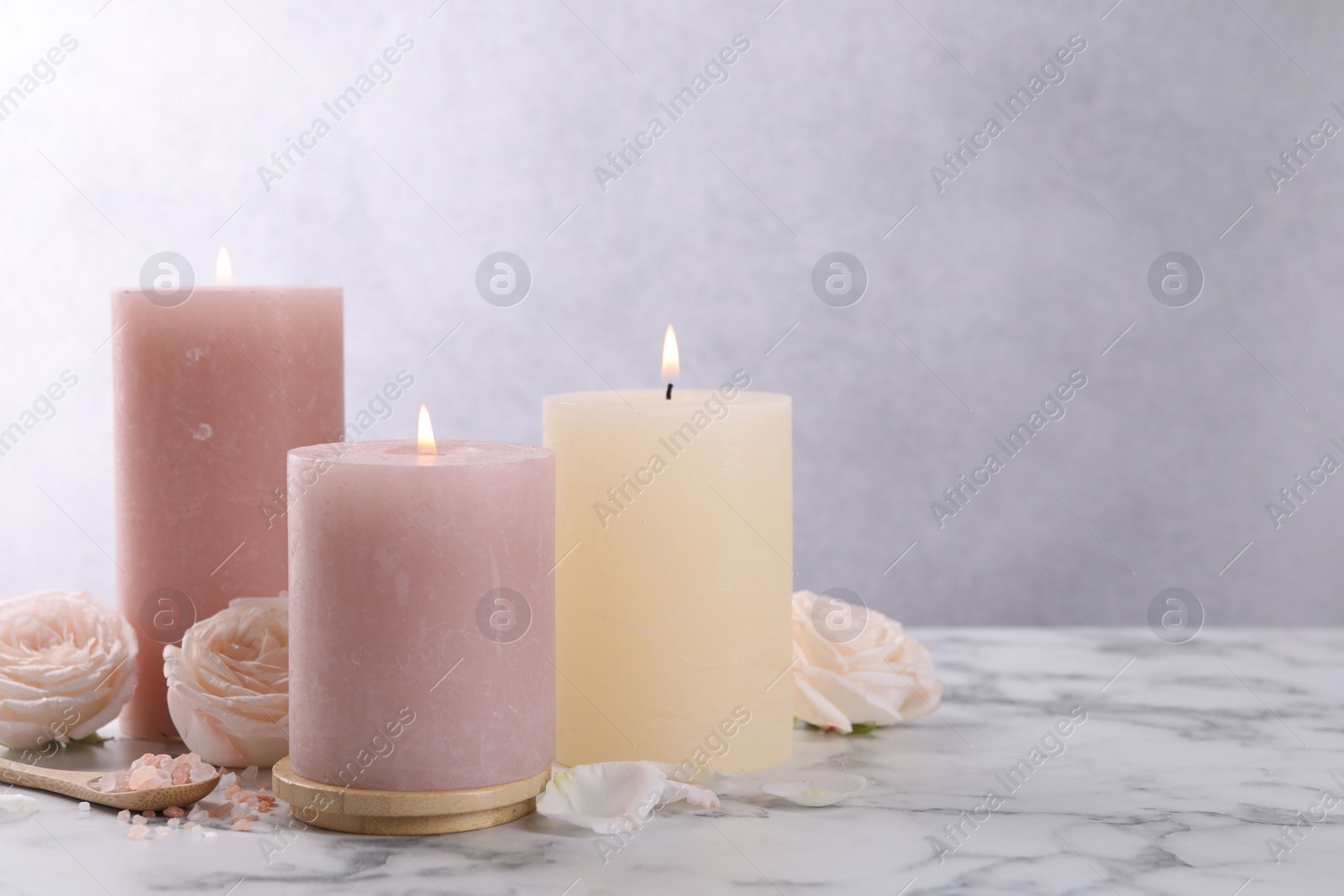 Photo of Spa composition with burning candles, flowers and sea salt on white marble table, space for text