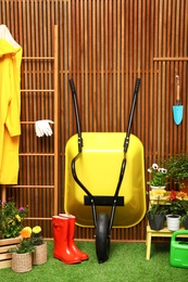 Photo of Gardening tools with wheelbarrow and flowers near wooden wall