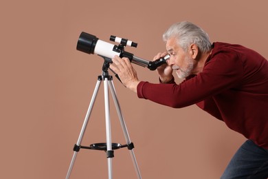 Senior astronomer looking at stars through telescope on brown background