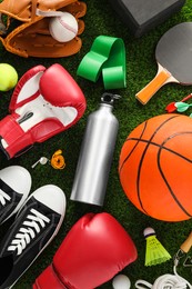 Photo of Different sport equipment and sneakers on green grass, flat lay