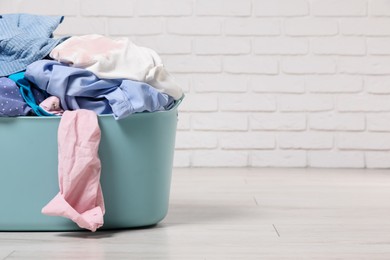 Photo of Laundry basket with clothes near white brick wall. Space for text