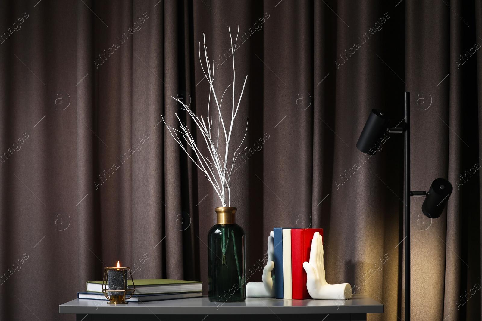 Photo of Vase with white tree twigs, books and candle on chest of drawers indoors