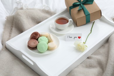 Photo of Tasty breakfast served in bed. Delicious macarons, tea, gift box, rose and I Love You card on tray